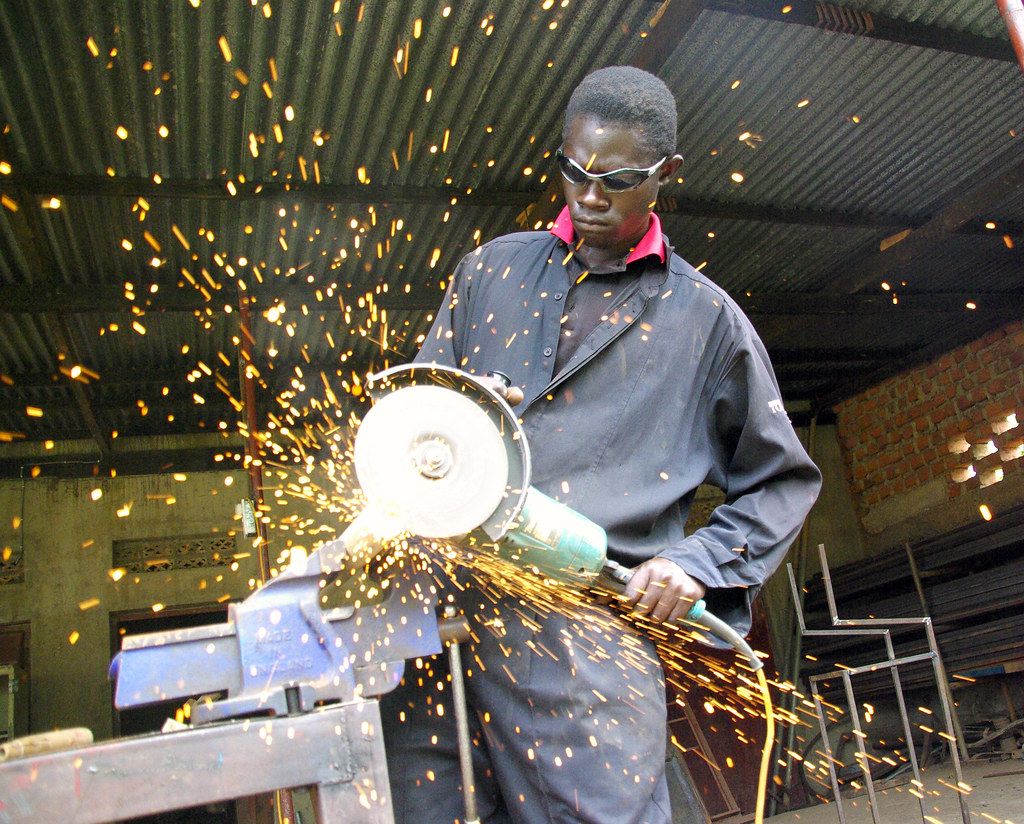 Fabricator angle-grinding a steel member, orange sparks flying