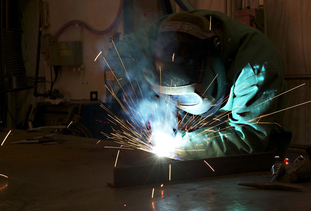 Welder joining steel components in a dark workshop, sparks scattering